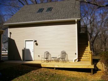 Side view of a custom garage addition with bonus room on second floor that also shows a deck and staircase between the home and the addition