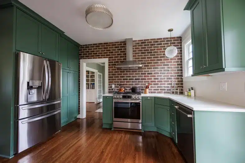 red brick kitchen wall with green cabinets and white countertop