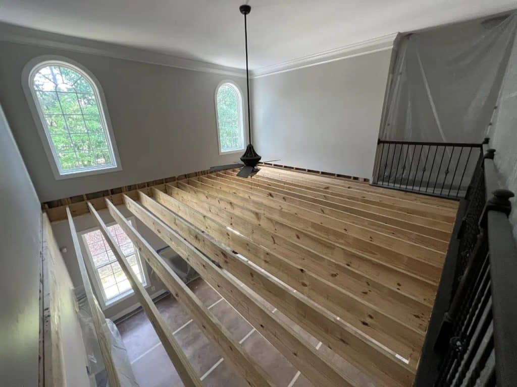 work in progress image of wooden beams beginning to close off a two story family room to create an extra room on the second level of the home