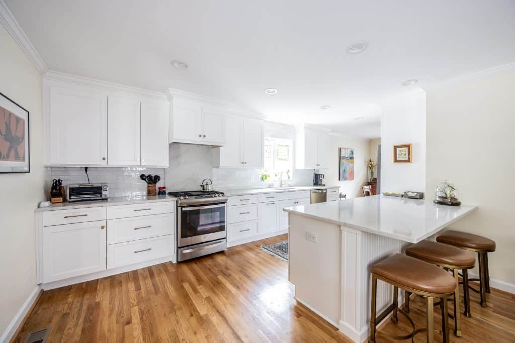 full view of kitchen with white cabinets and island with granite countertops and bar stools