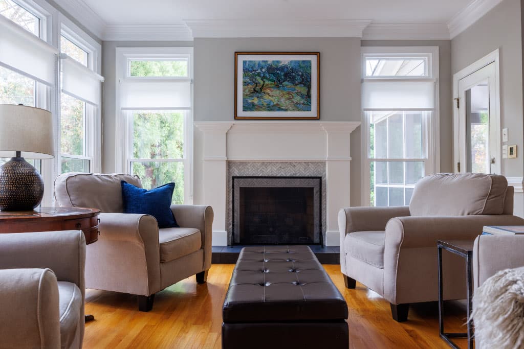 renovated living room with fireplace in between two floor to ceiling windows and arm chairs