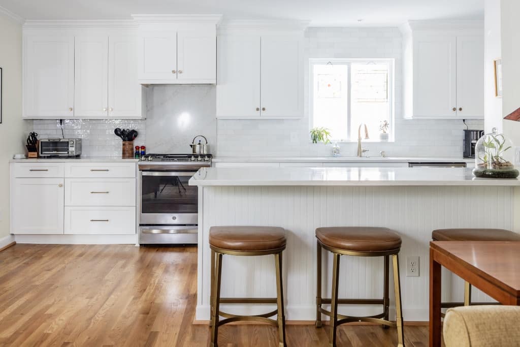 newly remodeled white cabinet and white quartz countertop kitchen with hardwood floors and leather barstools at the peninsula counter