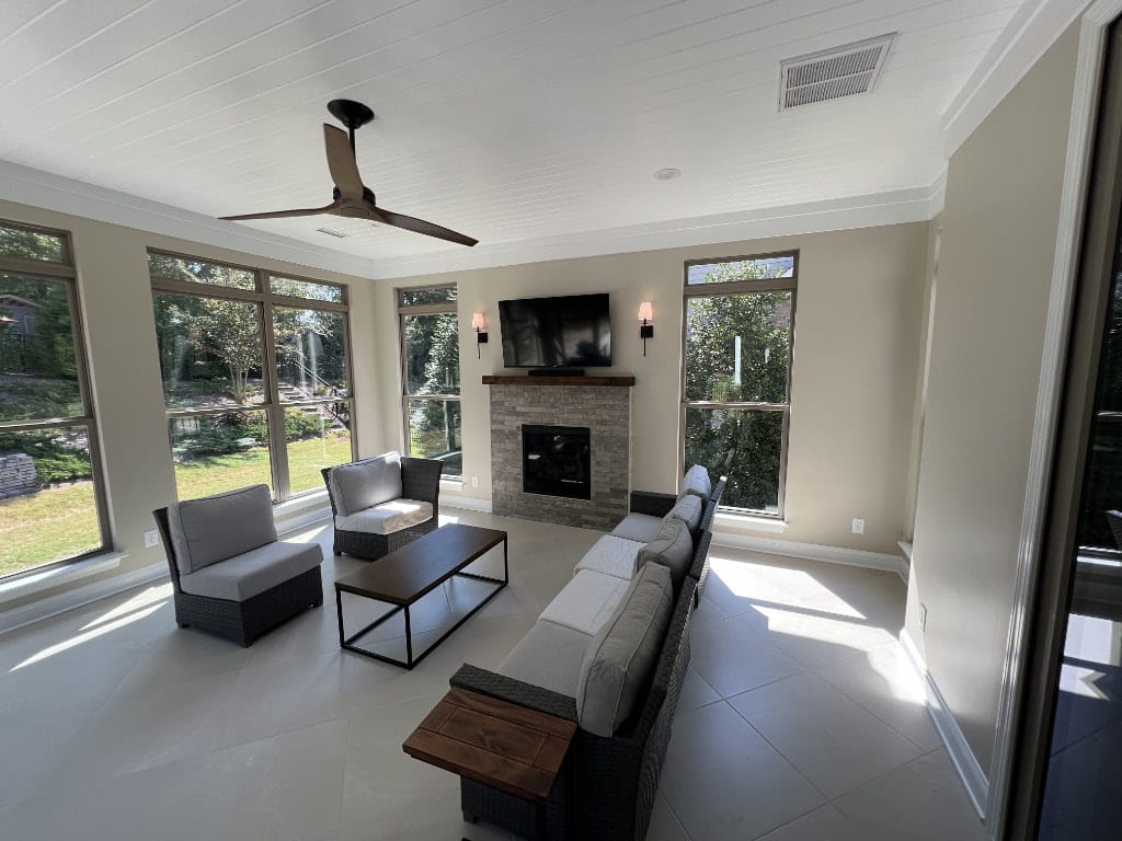interior of sunroom showing couches, cieling fan, floor to ceiling windows, and fireplace with tv