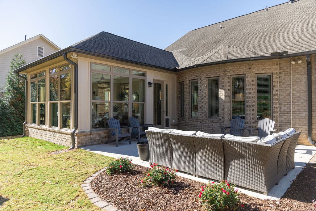 sunroom addition that opens out to a remodeled stone patio with adirondack chairs and cushioned patio couch looking at to newly landscaped yard