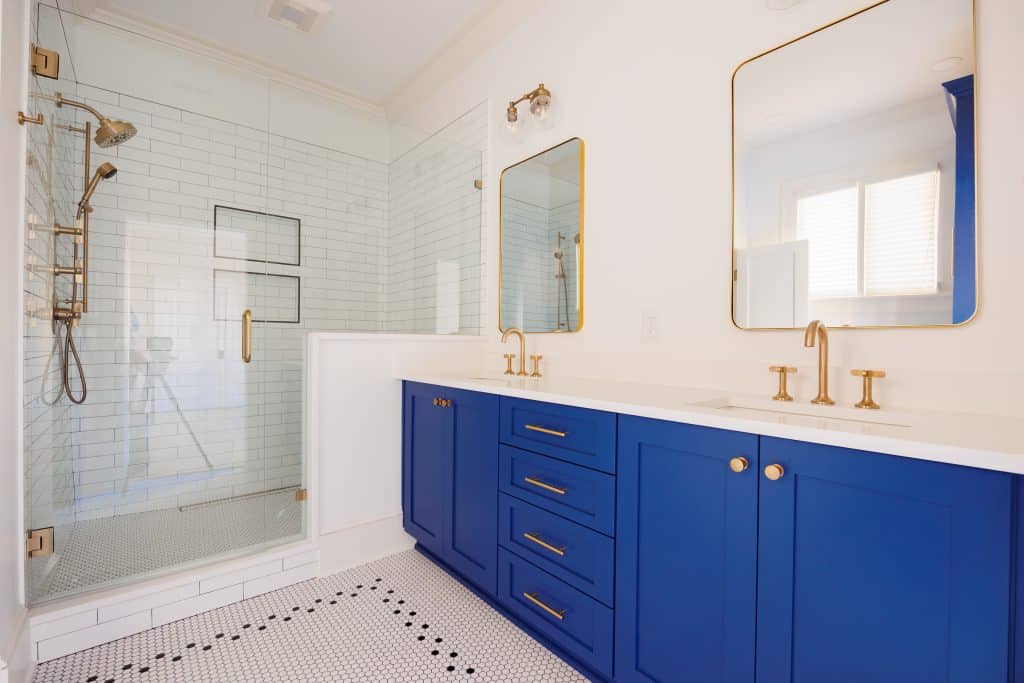 primary bath double sink vanity with walk in shower. blue vanity with gold faucets.