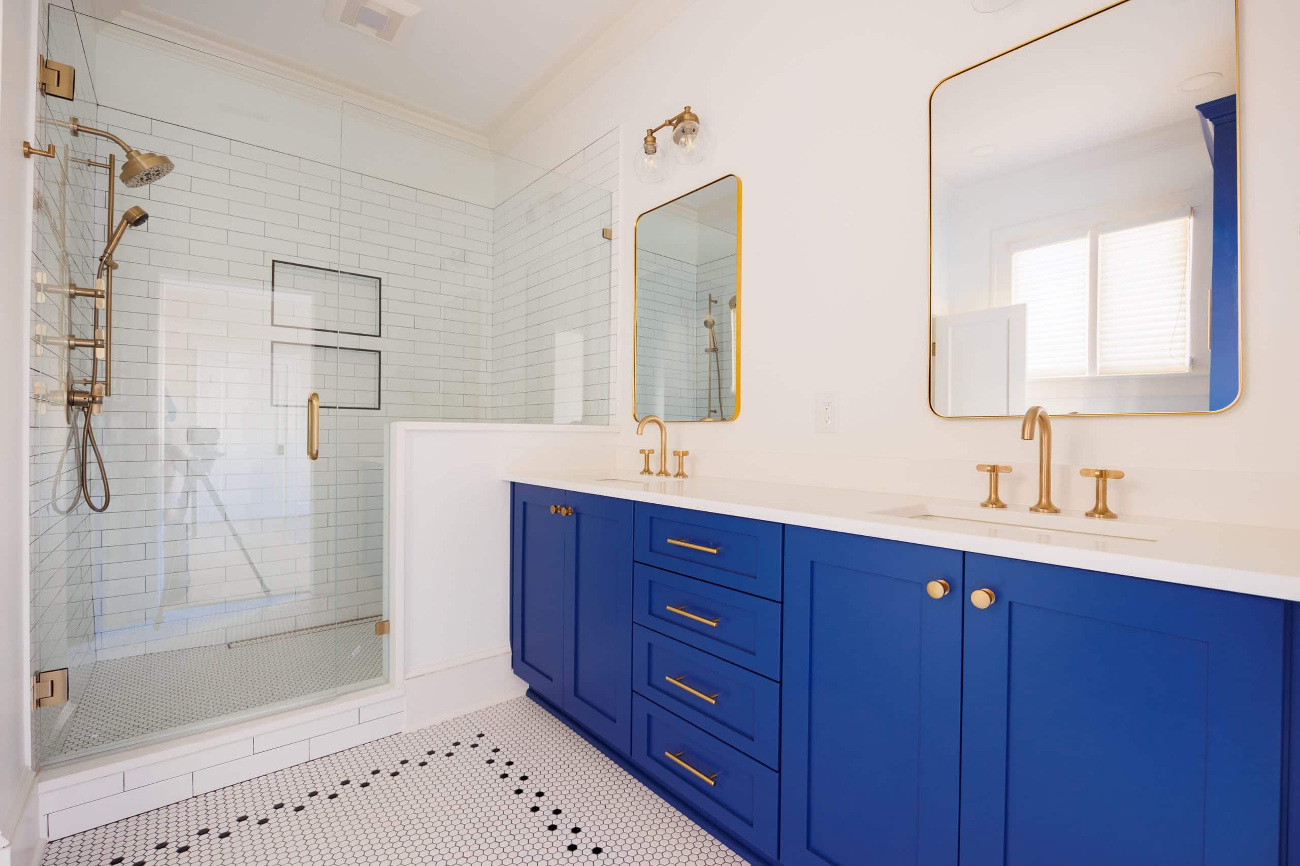 primary bath double sink vanity with walk in shower. blue vanity with gold faucets.
